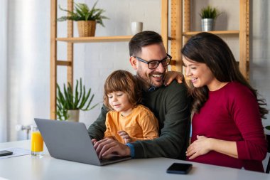 Çocuklu mutlu bir aile birlikte dizüstü bilgisayar kullanarak eğleniyor, ebeveynler ve çocuklar evde gülüyor bilgisayarla komik bir internet videosu izliyor, online arama yapıyor.