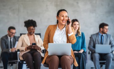 Ofiste yeni bir proje üzerinde çalışırken gülen iş adamları. Modern bir çalışma alanında çalışırken bilgisayar kullanan bir grup farklı iş adamı..