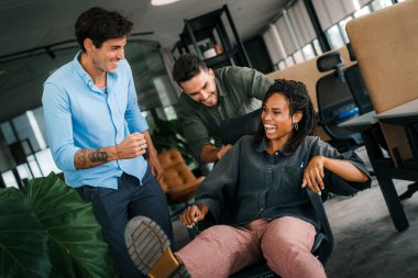 Genç iş arkadaşları birlikte eğleniyor, koltuklarda oturuyorlar, çeşitli heyecanlı ofis çalışanları tatilin tadını çıkarıyorlar, gülüyorlar, eğlenceli aktiviteler yapıyorlar, kurumsal başarıyı kutluyorlar..