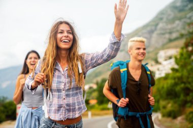 Neşeli ırklar arası arkadaşlar yol kenarında pankartlarla duruyorlar, otostop çekiyorlar, yaz tatilinde arabayı durduruyorlar. Turizm, birlikte seyahat, özgürlük ve arkadaşlık kavramı