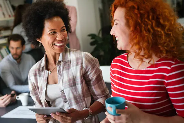 Dijital tablet bilgisayar kullanarak birlikte çalışan iki iş kadını bir iş projesi hakkında konuşuyor. Kadın yöneticilerden oluşan küçük yaratıcı çeşitlilik ekibi ofiste çalışıyor..