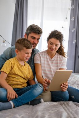 Çocuklu mutlu bir aile tablet bilgisayar kullanarak eğleniyor, ebeveynler ve çocuklar gülüyor evde bilgisayarla komik internet videoları izleyip, online arama yapıyorlar.
