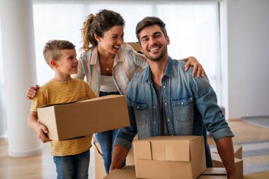 Taşındığı gün yeni evde karton kutuları olan mutlu bir aile. İpotek, aile ve gayrimenkul konsepti, mutlu anne, baba ve çocuk kutuları yeni eve taşınıyor.