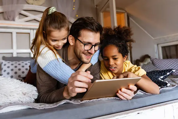 Mutlu çoklu etnik çeşitlilikte bir aile, baba ve çocuklar evde birlikte zaman geçiriyorlar ve dijital aletler kullanıyorlar..