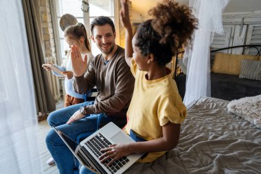 Tekerlekli sandalyedeki mutlu baba, iki farklı ırktan kızla birlikte dizüstü bilgisayar kullanıyor, liseli kız kardeşlerle birlikte gülümsüyor bilgisayar ekranına bakıyor, internetten alışveriş yapıyor.