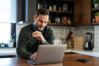 Doymuş modern adam elektronik bankacılık için dizüstü bilgisayar kullanıyor, rezervasyon yaptırıyor, online alışveriş yapıyor ve evde vakit geçirirken ödeme yapıyor..