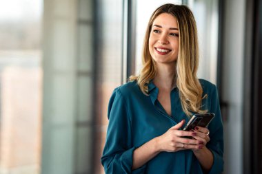 Genç, mutlu, zarif, profesyonel bir iş kadını. Yönetici ofisinde cep telefonu kullanıyor, cep telefonu tutuyor ve çalışıyor..