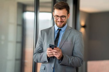 Şirket ofisinde haftalık programı analiz ederken cep telefonu kullanan mutlu bir iş adamı.