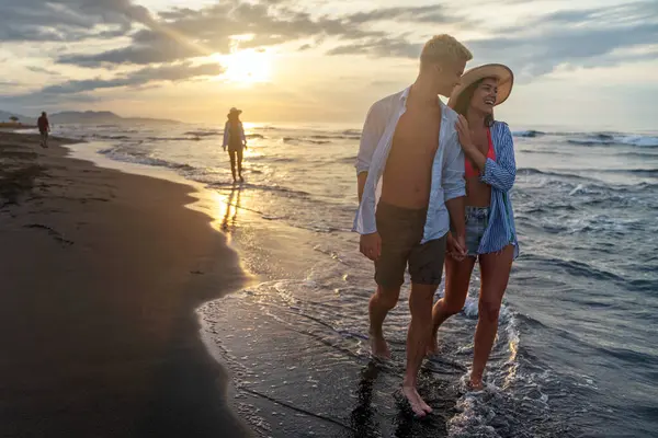 Kumsalda yürüyen bir çift. Genç mutlu ırklar arası çift kumsalda yürüyor gülümsüyor, yaz tatilinin tadını çıkarıyor, balayına çıkıyor.