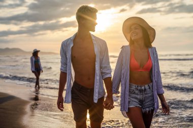 Kumsalda yürüyen bir çift. Genç mutlu ırklar arası çift kumsalda yürüyor gülümsüyor, yaz tatilinin tadını çıkarıyor, balayına çıkıyor.