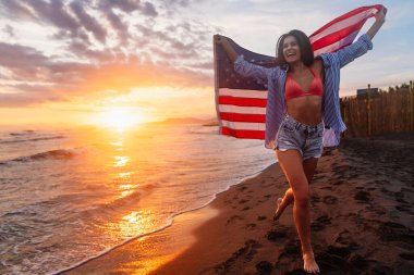 Okyanusta yürüyen Amerikan bayrağı taşıyan genç bir kadın. Amerika Bağımsızlık Günü konsepti. 4 Temmuz.