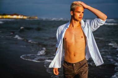 Kumsalda beyaz tişörtlü yakışıklı, genç ve yakışıklı bir adam. Huzur, rahatlık ve farkındalığın tadını çıkarıyor..