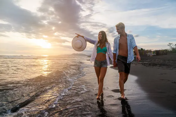 Kumsalda yürüyen bir çift. Genç mutlu ırklar arası çift kumsalda yürüyor gülümsüyor, yaz tatilinin tadını çıkarıyor, balayına çıkıyor.