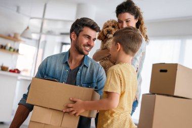 Taşındığı gün yeni evde karton kutuları olan mutlu bir aile. İpotek, aile ve gayrimenkul konsepti, mutlu anne, baba ve çocuk kutuları yeni eve taşınıyor.