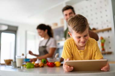 Mutfakta çocuklu mutlu bir aile birlikte modern tablet kullanarak eğleniyor, gülümseyen ebeveynler çocuklarla birlikte hafta sonunun keyfini çıkarıyor evde bilgisayardan gülen videolar izliyorlar.
