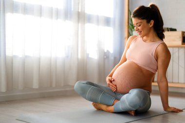 Huzurlu bir eyalette sakin bir hamile kadın yatak odasında doğum öncesi yoga yapıyor. Hamilelik, sağlıklı yaşam tarzı, spor kadını konsepti.