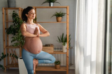 Aktif hamile kadın yoga yapıyor, kaslarını mindere geriyor, hamilelik öncesi egzersizleri yapıyor ve vücudu doğuma hazırlıyor.