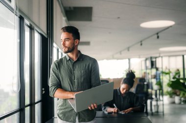 Yakışıklı, başarılı genç iş adamlarının portresi, ofiste dizüstü bilgisayarı olan bir yazılım mühendisi. Girişim, serbest çalışma, insanlar ve teknoloji konsepti.