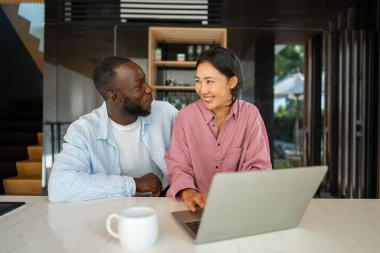 Aşırı mutlu çift dizüstü bilgisayar kullanıyor, satışlarla online alışveriş yapıyor, dijital ekrana bakarak oyun oynuyor. Mutlu Afrikalı Amerikalı erkek ve Asyalı kadın çevrimiçi piyango zaferini kazandı.