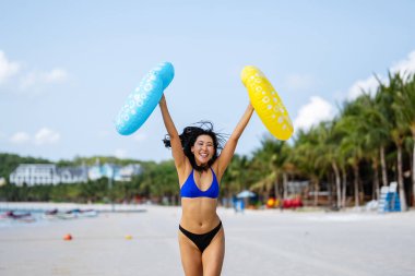 Özgür hissediyorum. Neşeli genç Asyalı bir kadın renkli şişme yüzüklerle ellerini kaldırarak mükemmel bir plaj tatilinin özgürlüğünü kutluyor.