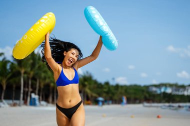 Mutlu genç bir kadın, eğlenceli bir plaj gününün tadını çıkarıyor, okyanus dalgalarında yüzüyor, güneşli gökyüzünün altında gülümsüyor, özgür ve tasasız bir tropikal tatilde.