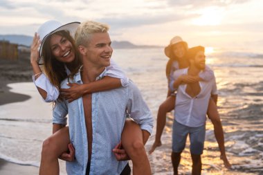 Bir grup mutlu arkadaş, sevgililer gün batımında sevgililerini sırtında taşıyorlar ve yaz tatilinin tadını çıkarıyorlar.