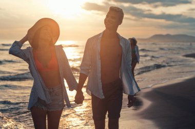 Kumsalda birlikte yürüyen tatilci çift birbirine sarılıyor. Mutlu ırklar arası genç çift yaz tatilinde balayının tadını çıkarıyor.