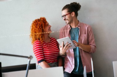 İki iş adamı dijital tablet bilgisayarı kullanarak birlikte çalışıyor ve bir iş projesi hakkında konuşuyorlar. Yöneticilerden oluşan küçük yaratıcı çeşitlilik ekibi ofiste çalışıyor..