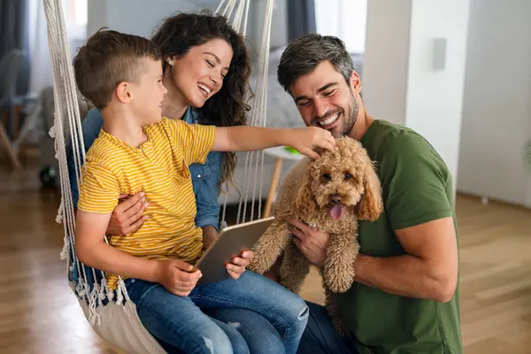 Çocuklu mutlu bir aile tablet bilgisayar kullanarak eğleniyor, ebeveynler ve çocuklar gülüyor dijital cihazla evde dinleniyorlar, komik internet videoları izliyorlar, online arama yapıyorlar.