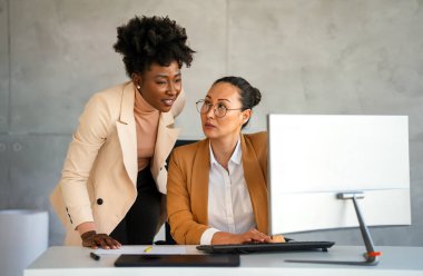 Modern bir ofiste hevesle çalışan mutlu profesyonel kadınlar. İki kadın girişimci şirket işyerindeki verimli bir iş toplantısı için bilgisayarı kullanıyor..