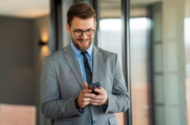 Ofiste cep telefonu kullanan mutlu orta yaşlı iş adamı yöneticisi. Gülümseyen iş adamı CEO yatırımcı elinde akıllı telefonuyla şirket ofisinde duruyor..