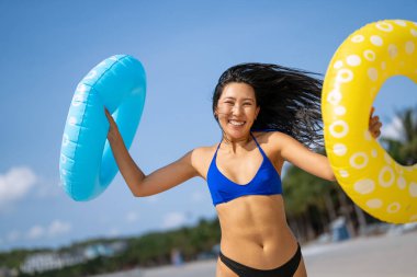 Mutlu genç bir kadın, eğlenceli bir plaj gününün tadını çıkarıyor, okyanus dalgalarında yüzüyor, güneşli gökyüzünün altında gülümsüyor, özgür ve tasasız bir tropikal tatilde.