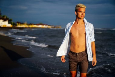 Yaz tatilinde tropik plajda dinlenen şık bir adam. Dertsiz, bronzlaşmış, denizde rahatlayan adamın portresi. Gülümseyen genç adam esintiden ve bakışlardan zevk alıyor..