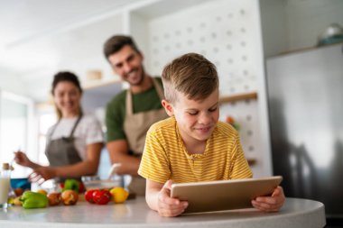 Çocuklu mutlu bir aile tablet bilgisayar kullanarak eğleniyor, ebeveynler ve çocuklar gülüyor dijital cihazla evde dinleniyorlar, komik internet videoları izliyorlar, online arama yapıyorlar.