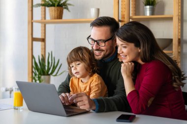 Çocuklu mutlu bir aile birlikte dizüstü bilgisayar kullanarak eğleniyor, ebeveynler ve çocuklar evde gülüyor bilgisayarla komik bir internet videosu izliyor, online arama yapıyor.