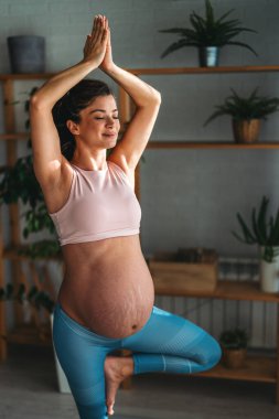 Evde çalışan hamile bir kadının portresi. Hamile kadın evde yoga yapıyor. Hamilelik yogası ve fitness.