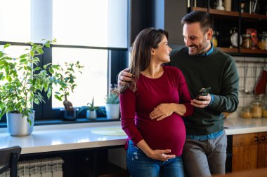 Birlikte telefon kullanan çok mutlu bir çift. Mutlu hamile kadın ve kocası selfie çekiyorlar, internette sörf yapıyorlar, akıllı telefonlar tutuyorlar, aletlerle eğleniyorlar, boş zamanların tadını çıkarıyorlar.