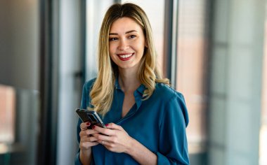 Şirket ofisinde haftalık programı analiz ederken cep telefonu kullanan mutlu bir iş kadını.