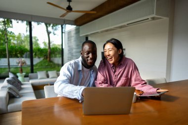 Aşırı mutlu çift dizüstü bilgisayar kullanıyor, satışlarla online alışveriş yapıyor, dijital ekrana bakarak oyun oynuyor. Mutlu Afrikalı Amerikalı erkek ve Asyalı kadın çevrimiçi piyango zaferini kazandı.