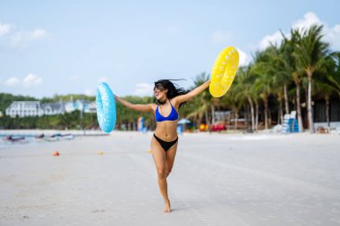 Nihai yaz titreşimleri. Genç bir kadın güneşin sıcaklığından zevk alır, şişme yüzükler tutar ve plaj hayatının keyfini çıkartır.