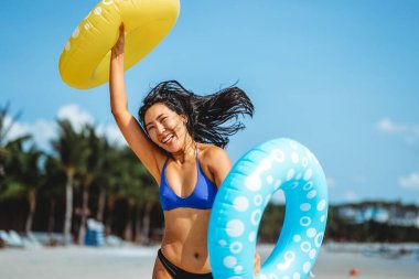 Özgür hissediyorum. Neşeli genç Asyalı bir kadın renkli şişme yüzüklerle ellerini kaldırarak mükemmel bir plaj tatilinin özgürlüğünü kutluyor.