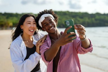 Mutlu ırklar arası bir çift tropik bir sahilde selfie çekiyor tatilin, uzak işin, sosyal medyanın nişanının ve kaygısız bir dijital yaşam tarzının tadını çıkarıyor.