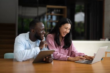 Genç ve çok ırklı çift evde bilgisayar ve dijital cihaz kullanırken eğleniyor. İnsanlar, teknoloji, online yaşam tarzı konsepti