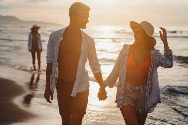 Genç ve güzel bir çift gün batımında deniz kıyısında yürüyor. Balayı. Romantik gezi..