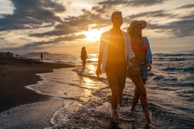 Kumsalda yürüyen bir çift. Genç mutlu ırklar arası çift kumsalda yürüyor gülümsüyor, yaz tatilinin tadını çıkarıyor, balayına çıkıyor.