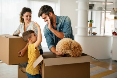 Taşındığı gün yeni evde karton kutuları olan mutlu bir aile. İpotek, aile ve gayrimenkul konsepti, mutlu anne, baba ve çocuk kutuları yeni eve taşınıyor.