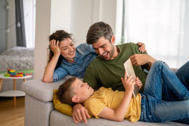 Çocuklu mutlu bir aile tablet bilgisayar kullanarak eğleniyor, ebeveynler ve çocuklar gülüyor evde bilgisayarla komik internet videoları izleyip, online arama yapıyorlar.