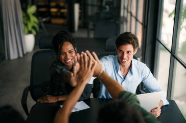 Neşeli iş adamları tezahürat yapıyor, iyi satış sonuçlarını kutluyor ve finansal hedefe ulaşıyor. Neşeli meslektaşlar modern ofiste başarıyı kutlarken gülerler..