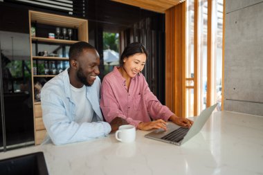 Evde dizüstü bilgisayarlı, yatırım, tasarruf ve faturalar için bütçe planlayan çok ırklı mutlu çift. Çevrimiçi bankacılık ve çeşitli, çok ırklı karı ve kocalarla finansal ödeme