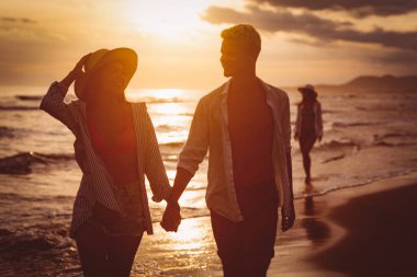 Kumsalda yürüyen bir çift. Genç mutlu ırklar arası çift kumsalda yürüyor gülümsüyor, yaz tatilinin tadını çıkarıyor, balayına çıkıyor.